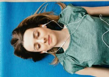 Young woman meditating with closed eyes on a yoga mat, listening to music.
