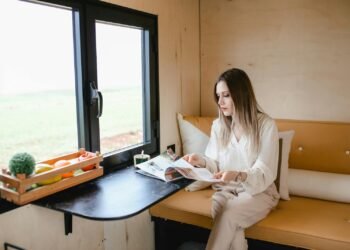 Woman reading magazine in a cozy tiny house with a scenic view.