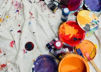 assorted-color paints and paintbrushes on white tarp