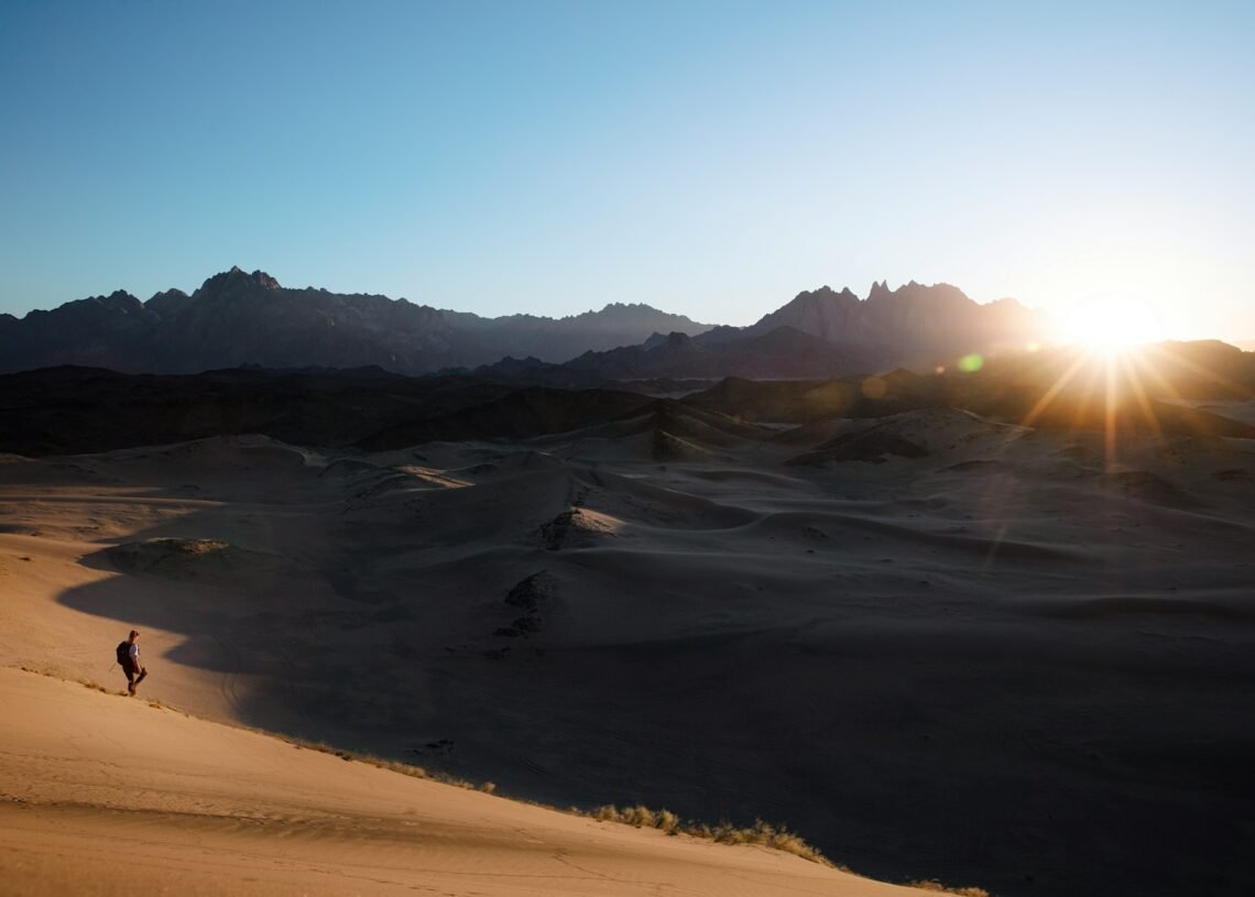 a person is walking in the desert at sunset