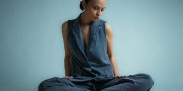 A woman in a vest and pants sits cross-legged.