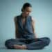 A woman in a vest and pants sits cross-legged.