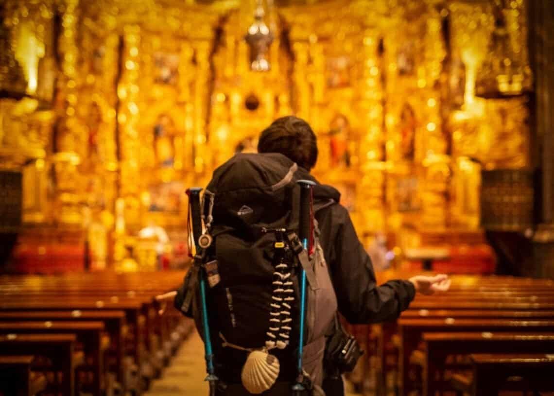 Pilgrim with backpack facing ornate church altar