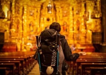 Pilgrim with backpack facing ornate church altar