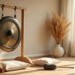 Gong en bronze suspendu à un support en bois dans une pièce calme, coussins au sol et lumière du matin : bain de gong